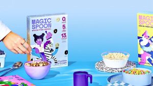 box of keto friendly cereal and bowls filled with purple cup on table