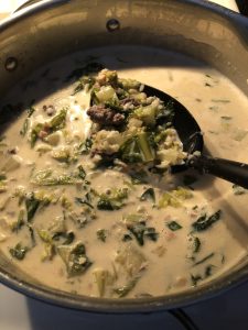 creamy sausage and greens soup in silver pot with large black spoon