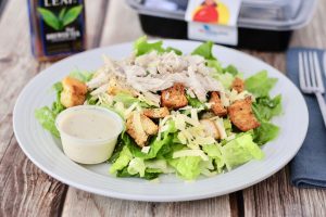 pieces of chicken on bed of lettuce with dressing in container on side of the plate